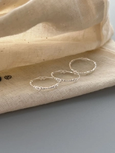 Detailed close-up of three silver bow rings with beaded texture on a linen bag