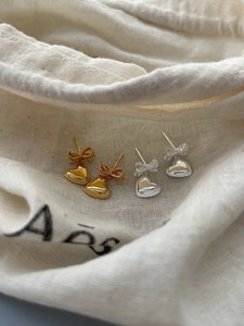 Détail de boucles d'oreilles nœud et cœur en argent S925 doré et argenté sur lin