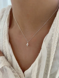 Detail of silver geometric diamond pendant necklace worn over a white lace garment