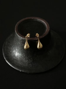 Close-up of golden teardrop stud earrings on a dark ceramic display stand