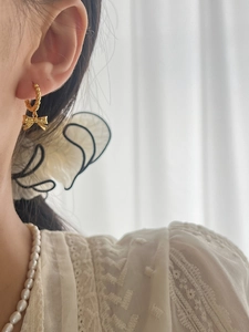 Detail of elegant gold bow pendant earring worn by a model with a pearl necklace