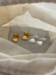 Détail de boucles d'oreilles nœud et cœur en argent et or dans un pochon en lin