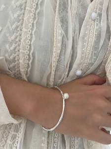 Detail eines silbernen Bambus-Armreifs mit einer glänzenden weißen Perle am Handgelenk