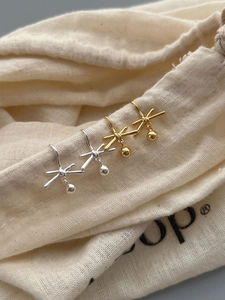 Detail of silver and gold bow earrings with spherical pendants on a linen pouch