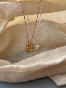 Detail of silver and gold heart key necklaces on a textured fabric bag surface