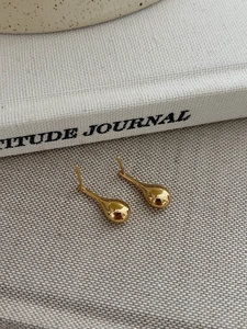 Polished gold teardrop stud earrings displayed on a minimalist grey fabric and book