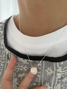 Détail du collier pendentif camélia argenté avec perle blanche sur le cou d'un modèle