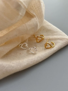 Macro shot of minimalist hollow heart hoop earrings in gold and silver finish with linen pouch