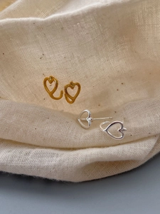 Macro shot of gold and silver hollow heart earrings on textured beige linen fabric
