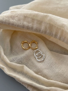 Macro detail of textured gold and silver S925 sterling silver hoop earrings on linen cloth