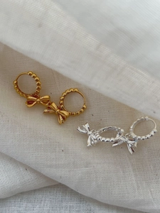 Detail of 925 sterling silver bow earrings in gold and silver finish on linen