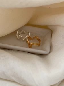 Détail macro de bagues ondulées or et argent sur un plateau en céramique minimaliste
