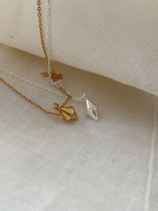 Detail of minimalist gold and silver geometric cone pendants on soft linen fabric