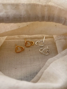 Detail shot of hollow heart silver earrings in gold and silver finish on soft fabric