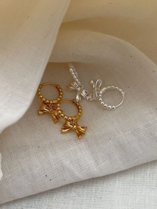 Macro view of sterling silver bow earrings in gold and silver finish on soft fabric
