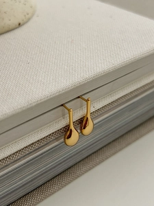Close-up of teardrop stud earrings in polished gold finish on linen texture background
