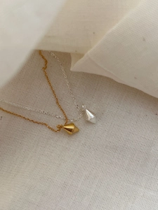 Detail of minimalist gold and silver geometric diamond pendant necklaces on soft linen