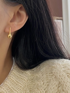 Close-up of a minimalist gold teardrop earring worn by a model in a warm knit sweater
