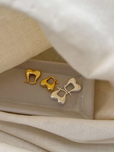 Detailed view of chunky heart-shaped earrings in gold and silver on a ceramic tray