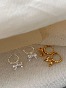 Detail of silver and gold bow drop earrings with textured hoops on fabric