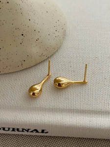 Detailed close-up of polished gold teardrop stud earrings with smooth mirror finish