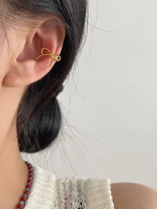 Detailed view of a gold bow-shaped ear cuff with delicate beaded texture on a model