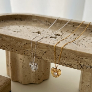 Elegant gold and silver heart necklaces with sunburst texture and zircon on travertine