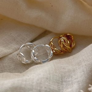 Boucles d'oreilles torsadées en argent et or sur fond de tissu minimaliste