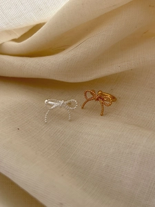 Detailed view of silver and gold bow earrings with intricate woven texture on linen
