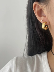 Close-up of gold C-shaped hoop earrings with double row zircon on a female model