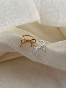 Detailed view of silver and gold bow ear clips with elegant twisted texture on linen fabric