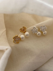Detail of silver and gold floral stud earrings with white pearls on soft textured fabric