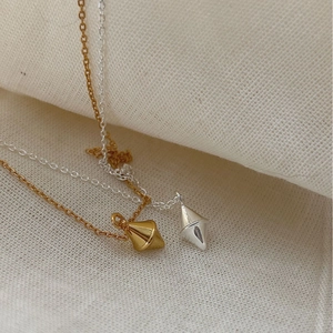 Minimalist gold and silver geometric diamond pendant necklaces on neutral fabric background