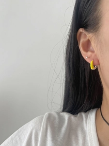 Detailed close-up of yellow enamel crescent earrings worn on the earlobe with silver finish