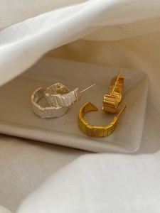 Close-up of gold and silver C-shaped earrings with vertical stripes and tiny inset crystals