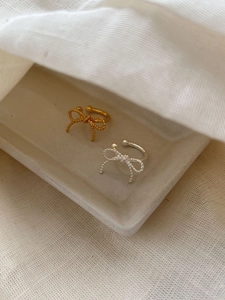 Detail of silver and gold bow ear cuffs with rope texture on a white decorative tray