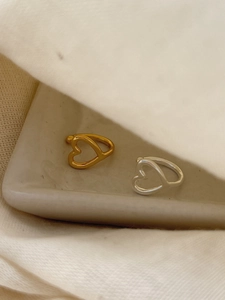 Close-up of gold and silver hollow heart earrings on a ceramic tray with soft fabrics