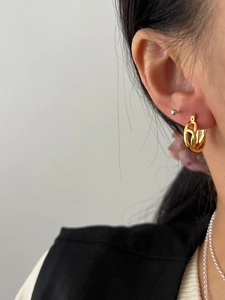 Close-up of golden intertwined Mobius loop earrings worn with elegant accessories