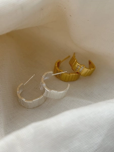 Detailed view of silver and gold C-shaped earrings with striped texture and small zircons