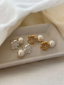 Detail of elegant silver and gold flower pearl earrings with zircon inlay on a white tray