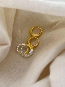 Detail of silver and gold huggie earrings with yellow enamel finish on textured fabric