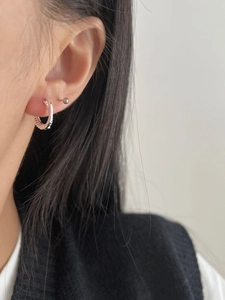 Macro shot of twisted silver hoop earrings and a minimalist ball stud on a model ear