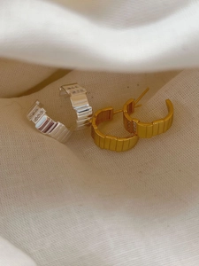 Close-up of gold and silver C-shaped earrings with vertical grooves and rectangular zircons