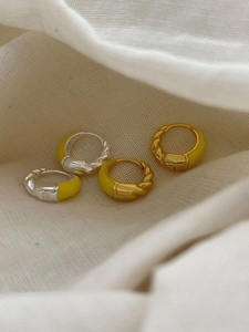 Detail of twisted rope silver earrings with yellow enamel finish on white fabric