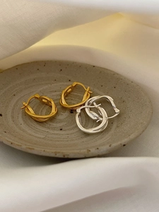 Detailed macro view of interweaving gold and silver hoop earrings on a ceramic dish
