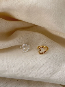 Detailed view of hollow heart-shaped ear cuffs in gold and silver on soft beige fabric