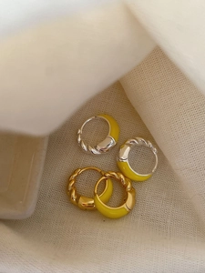Detail of twisted silver and gold hoop earrings with vibrant yellow enamel finish
