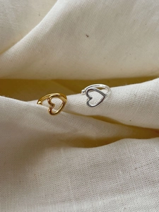 Detail of hollow heart ear cuffs in silver and gold on a textured fabric background