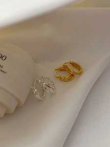 Macro detail of gold and silver braided chain style hoop earrings on white fabric