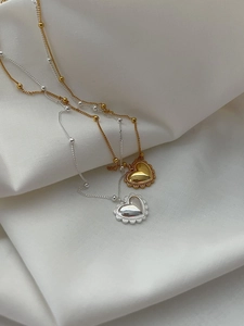 Détail de colliers cœur en or et argent avec bords festonnés sur tissu blanc plissé